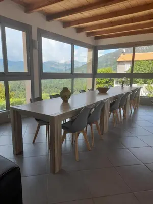 a long wooden table and chairs in a room with windows at Chambres d'Hôtes Villa Cardellini in Aullène