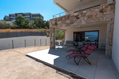 a patio with red chairs and a table on a building at L'Aurore de Cruciata - Appt vue baie d'Ajaccio in Pietrosella
