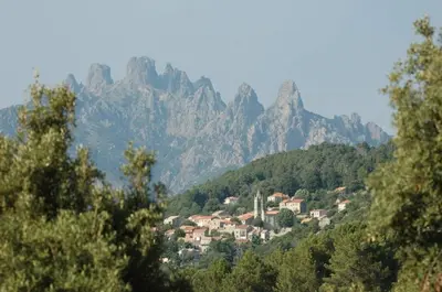 a village on a hill with mountains in the background at Hôtel Restaurant L'Aiglon in Zonza