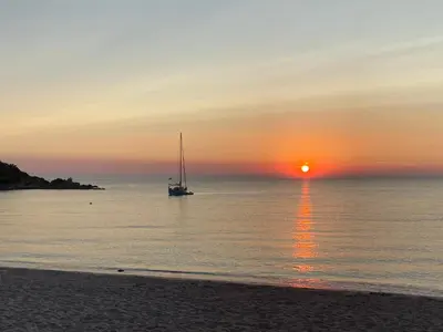 a sail boat in the ocean at sunset at Les Lodges de la Plage U Dragulinu in Sari Solenzara