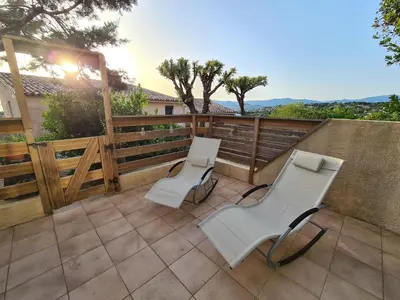 a patio with two white chairs and a fence at Studio avec terasse vue mer in Porticcio