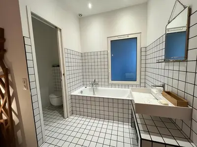a white tiled bathroom with a tub and a window at Appartement de maître T3 80m2 en plein centre. in Ajaccio
