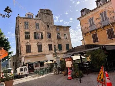 a street with two tall buildings with tables and chairs at Joli appartement F2 centre ville de Corte in Corte
