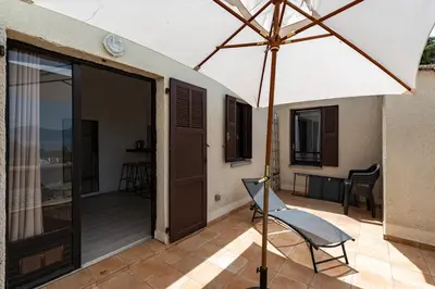 a patio with an umbrella and a chair on a porch at Le Paesolu in Grosseto-Prugna