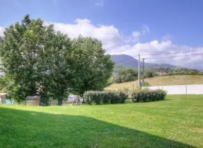 a green field with a tree and some bushes at Appartement tranquille en bas de villa in Afa