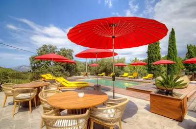 a patio with a table with red umbrellas and a pool at Hôtel Casale Olmia in Moncale