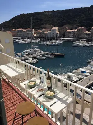 a table with a bottle of wine on a balcony with boats at Appartement duplex plein sud sur le port de Bonifacio in Bonifacio
