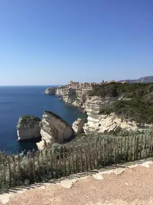 a fence on the side of a cliff near the ocean at Appartement duplex plein sud sur le port de Bonifacio in Bonifacio