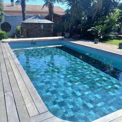 a swimming pool with blue tiles in a yard at Chalet - Piscine - Wifi in Penta-di-Casinca