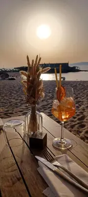 a table with a drink and a vase of flowers on the beach at face à la mer in Propriano