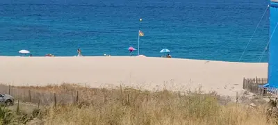 a beach with people and umbrellas in the water at face à la mer in Propriano