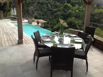 a dining table and chairs on a patio with a pool at Villa St Exupery in Oletta