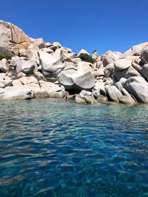 a person swimming in the water near some rocks at Villa Alivu belle piscine chauffée in Bonifacio