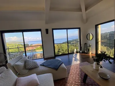 a living room with a couch and a table and windows at Magnifique villa vue mer avec piscine in Coti-Chiavari