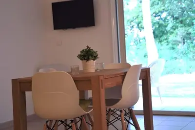 a dining room table with white chairs and a television at Appartement charmant en Corse avec terrasse au calme in Santa-Lucia-di-Moriani