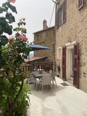 a patio with a table and chairs and a blue umbrella at Maison de caractère rénovée Coggia in Coggia