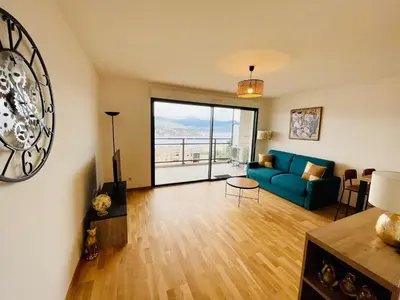 a living room with a blue couch and a large window at Ajaccio T2 grand standing neuf vue mer centre-ville & plages in Ajaccio