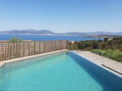 a large blue swimming pool next to a wooden fence at Villa ARIA, piscine, vue mer 120 m2 tout confort - 4 personnes in Pietrosella