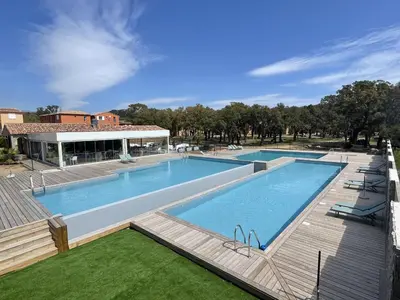 a large swimming pool with a wooden deck next to a building at Résidence hôtelière les hameaux de saint cyprien appartement 35 M2 1 chambre in Lecci