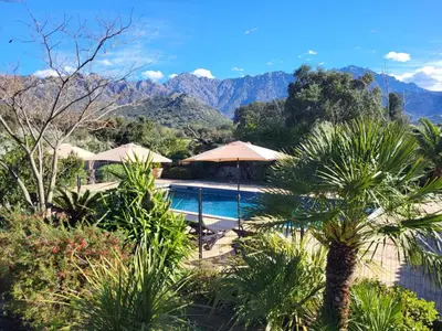 a resort with a pool and mountains in the background at Domaine du Reginu in Santa-Reparata-di-Balagna