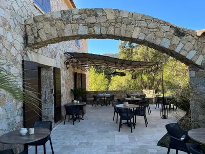 an outdoor patio with tables and chairs and a stone wall at Domaine du Reginu in Santa-Reparata-di-Balagna