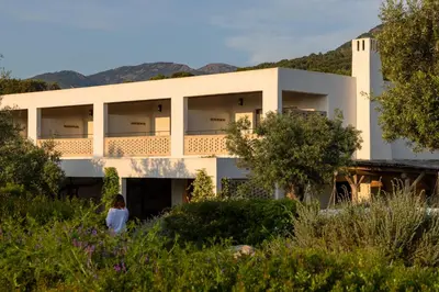 a woman walking in front of a white building at VILLA FLAKA Boutique Hôtel Wellness in Cargèse