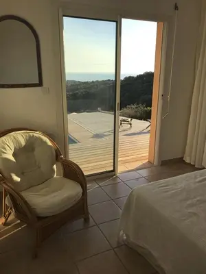 a bedroom with a bed and a chair and a sliding glass door at Modern villa 5 double bedrooms, new AC, private pool and stunning view 800 m from beach in Sagone