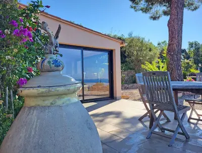 a table and a chair in a patio with a window at Les Terrasses du Pano - 95 m2 au calme - Jardin - Barbecue - Transats - Pleine vue mer - Wifi Fibre in Porticcio