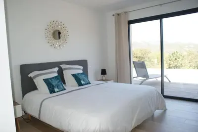 a white bedroom with a large bed and a balcony at Villa neuve avec grande piscine chauffée vue mer in Conca