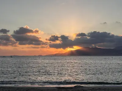 a sunset over the ocean with mountains in the background at Corse - Bord de mer, Appartement neuf avec Piscine Chauffée in Linguizzetta