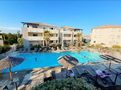 a large swimming pool with chairs and umbrellas at Corse - Bord de mer, Appartement neuf avec Piscine Chauffée in Linguizzetta
