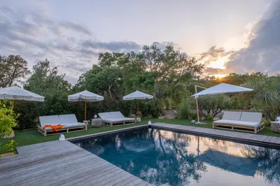 a swimming pool with two chairs and umbrellas next to at Villa Bambou 12 pers piscine chauffée 10 minutes à pieds plage in Sainte-Lucie de Porto-Vecchio