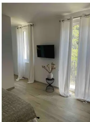 a bedroom with white curtains and a tv and a bed at Chambre avec balcon à louer in Bains de Guitera
