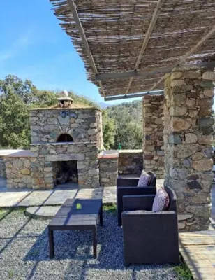 a patio with a stone fireplace with two chairs and a table at Maison en pierre corse avec vue entre mer et montagne in Moltifao
