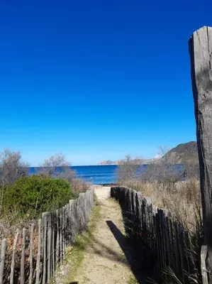 a dirt road next to a fence and water at Charmant petit logement à 3 kms de la plage in Belgodère