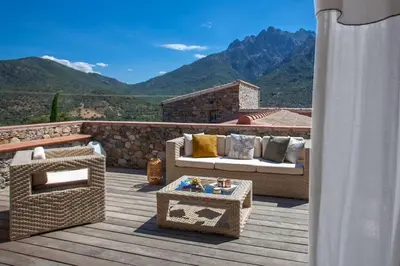 a patio with couches and a table on a deck at Maison en pierre Corse avec vue proche des Gorges de l'Asco entre mer montagne et piscine in Moltifao