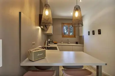 a kitchen with a white counter with two pink stools at Maison en pierre Corse avec vue proche des Gorges de l'Asco entre mer montagne et piscine in Moltifao