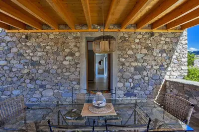 a patio with a table and chairs and a stone wall at Maison en pierre Corse avec vue proche des Gorges de l'Asco entre mer montagne et piscine in Moltifao
