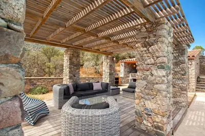 a patio with a stone wall and a wooden pergola at Maison en pierre Corse avec vue proche des Gorges de l'Asco entre mer montagne et piscine in Moltifao
