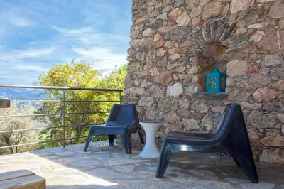 two chairs sitting on a patio with a stone wall at Le SAN PETRONE-TOUR EN PIERRE EN CENTRE CORSE ENTRE MER ET MONTAGNE in Moltifao
