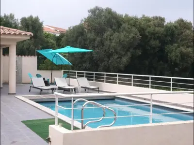 a swimming pool with chairs and a blue umbrella at Villa climatisée avec piscine in Sari Solenzara