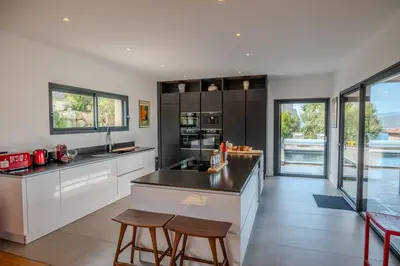 a kitchen with white cabinets and a counter with stools at Villa Terra Bella hauteur de la ville avec piscine et vue mer in Propriano