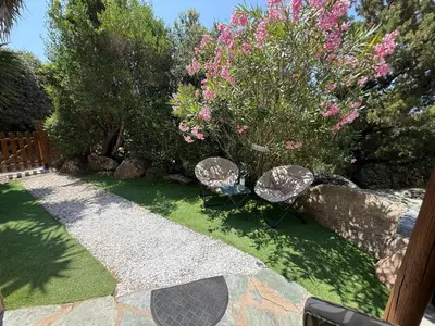 a garden with two chairs and a bush with pink flowers at Studio de charme à 300 m de la Plage de Santa Giulia in Porto-Vecchio