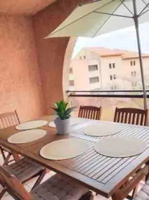 a wooden table with plates and an umbrella on a balcony at Le Cocon de Lilie in San-Nicolao