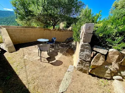 a patio with a table and chairs next to a stone wall at Casa Jeannot typique Corse en pierre, UNIQUEMENT DE SAMEDI EN SAMEDI , 2 pers, f2, 35 m2, jardin 60m2 vue montagne, parking in Monacia-dʼAullène