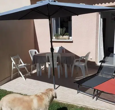 a dog standing next to a table with an umbrella at Les villas de Mélody in Santa-Maria-Poggio