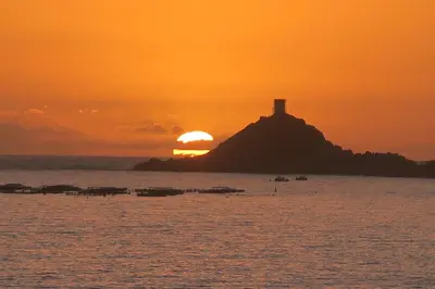 a sunset over a small island with a lighthouse on it at STUDIO LES CALANQUES in Ajaccio