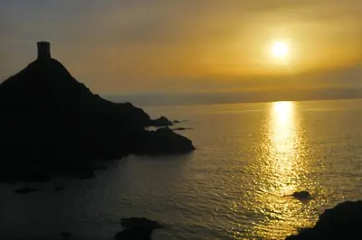 a sunset over the ocean with a lighthouse on a hill at STUDIO LES CALANQUES in Ajaccio