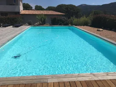 a large blue swimming pool with a wooden deck at Mini villa proche des plus belles plages in Porto-Vecchio
