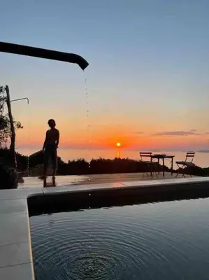 a man standing next to a swimming pool with the sunset at Casa Altura in Coti-Chiavari